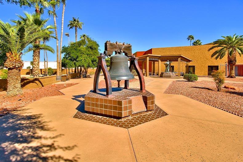 Photo of a large bell in the center of Sun City, Arizona with the main clubhouse in the background