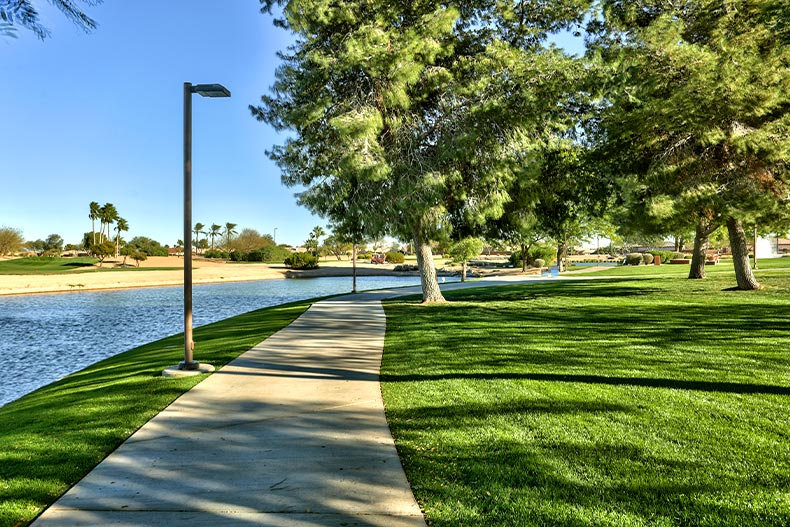 A paved walking and biking trail cutting through green grass near a pond in Sun City Grand, located in Surprise, Arizona