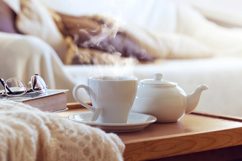 A sweater, book, and cup of tea with steam on on a wooden coffee table