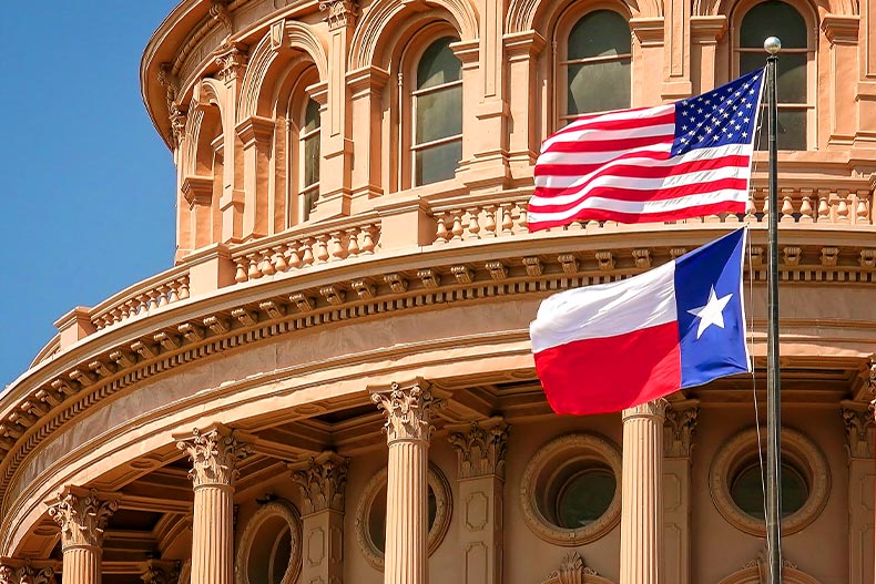 Exterior close-up photo of the Texas State Capitol in Austin, Texas with the Texas State Flag and US Flag in front