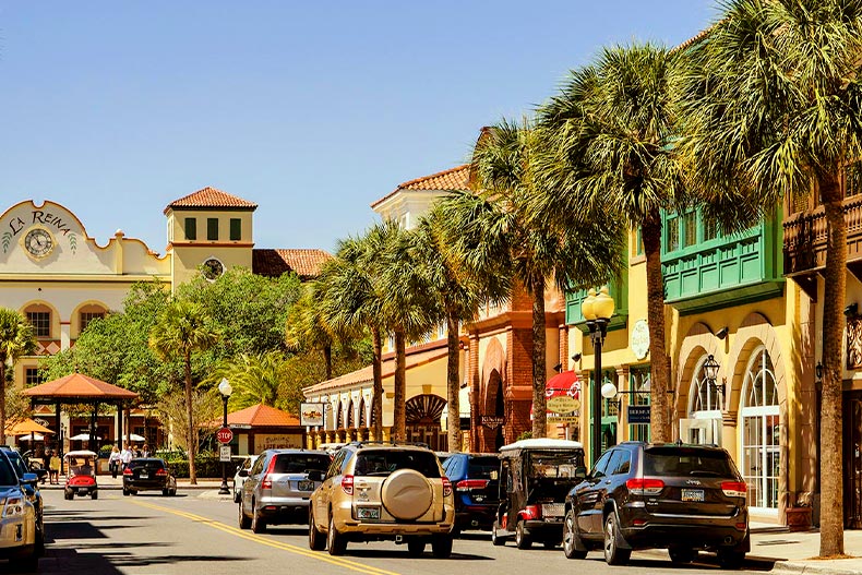 Photo a The Villages, Florida street lined with shops and palm tress. Cars and golf carts drive towards the La Reina building