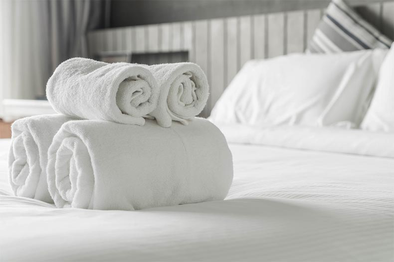 Fresh white towels rolled up on a bed with fresh sheets