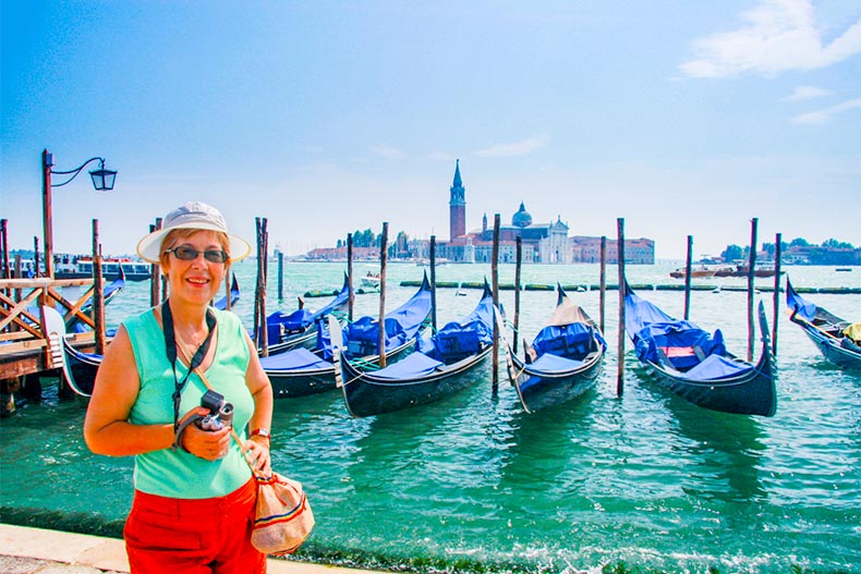 Senior woman stands in front of gondolas at a dock in Venice, Italy