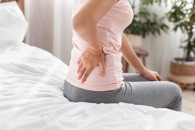 An older woman sitting on her bed at home and grabbing her lower back