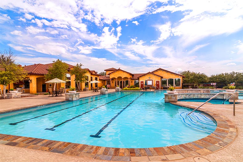A resort-style swimming pool with lap lanes in front of a yellow clubhouse in the Village at Tuscan Lakes, League City, Texas