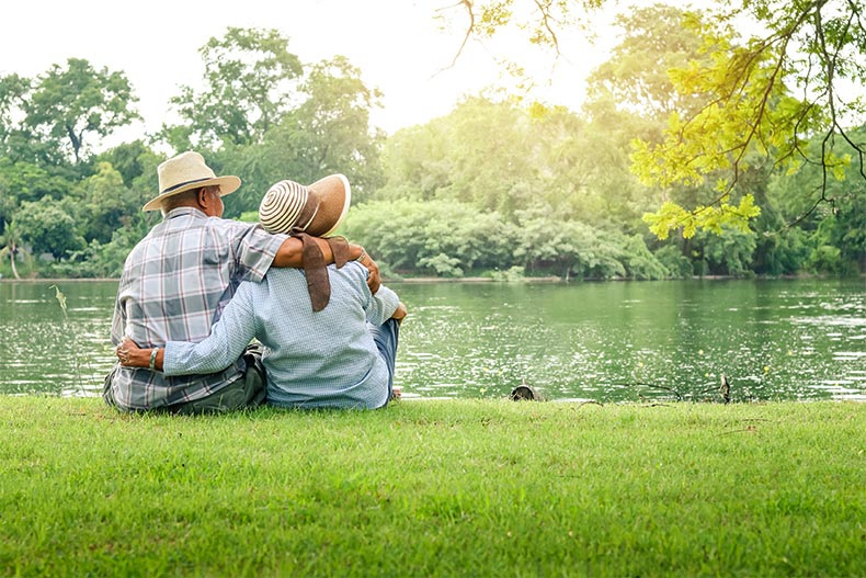 An older couple with their arms around each other sitting on the back of a picturesque river