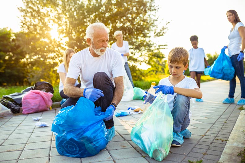 Older man and child volunteering by picking up garbage in a park