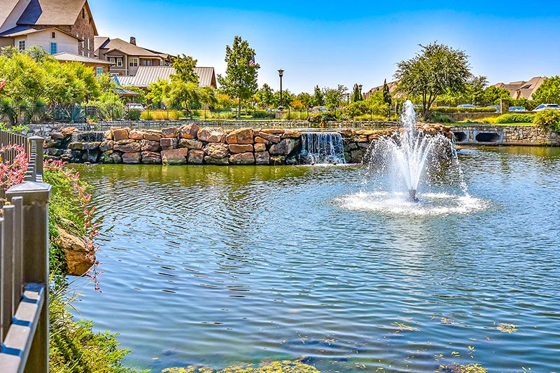 View of the pond with fountain and landscaping surrounding it with homes in the background.