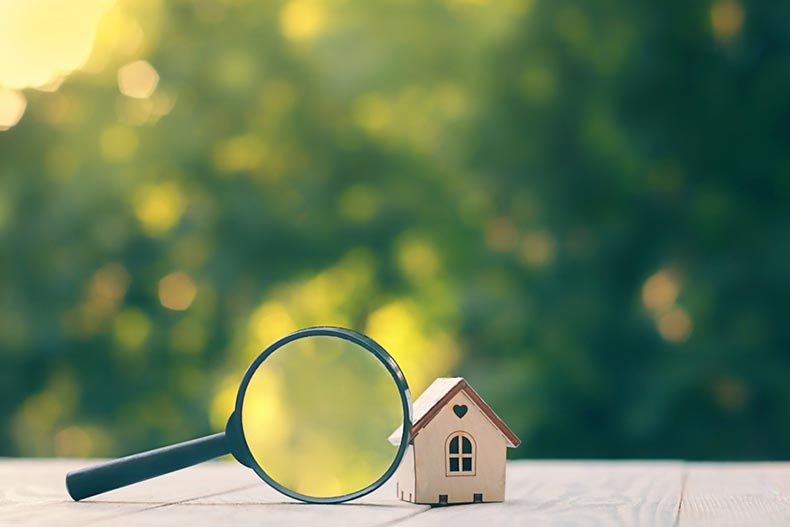 A magnifying glass beside a tiny model house on a wooden table