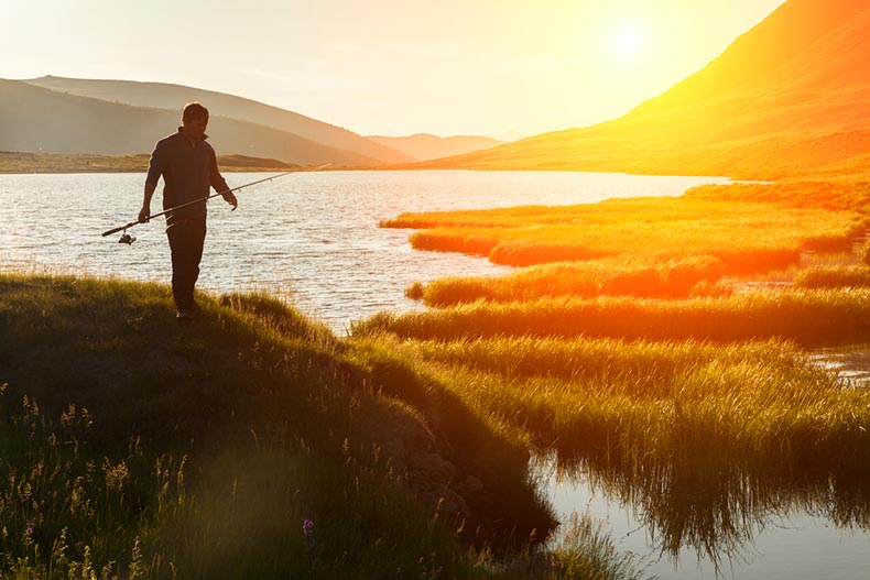 Silhouette of a fisherman with a fishing rod on the bank of the river