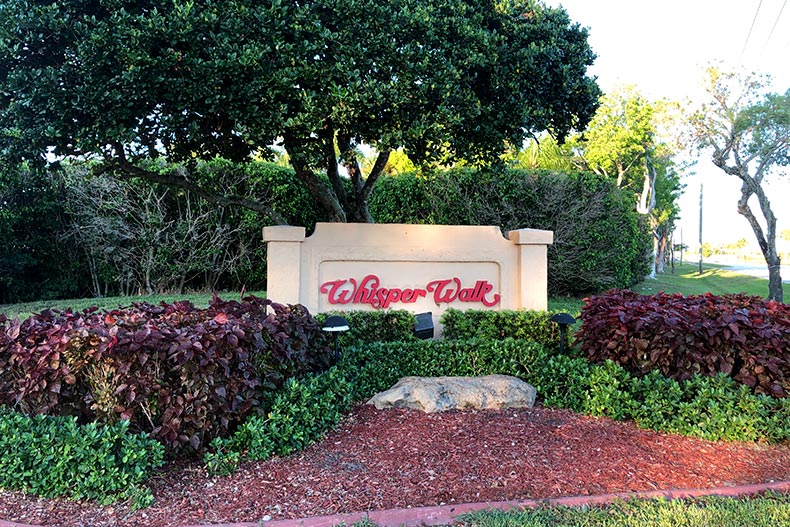 View of the community sign for Whisper Walk surrounded by shrubbery, located in Boca Raton, Florida
