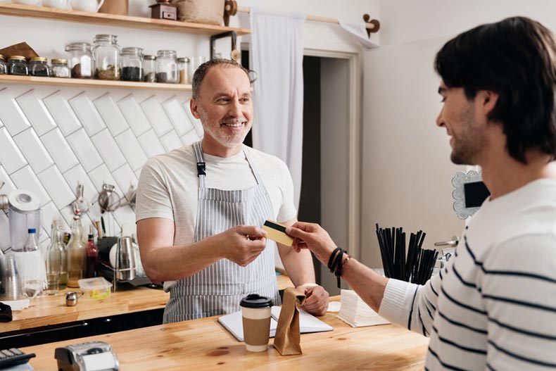 An older man accepting a credit card from a customer at a cafe