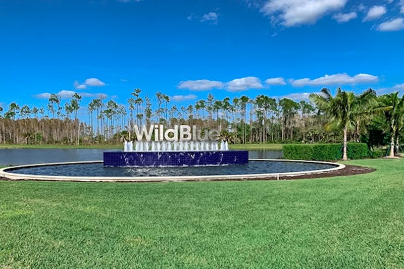 Entrance sign to the WildBlue with a water feature and plam trees in the background.