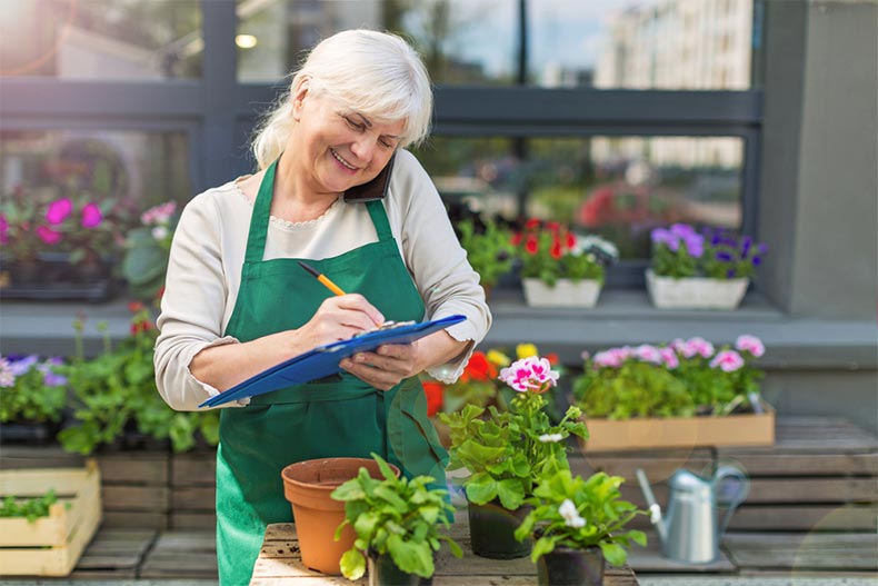 A senior woman smiling while on the phone and writing down orders at a flower shop