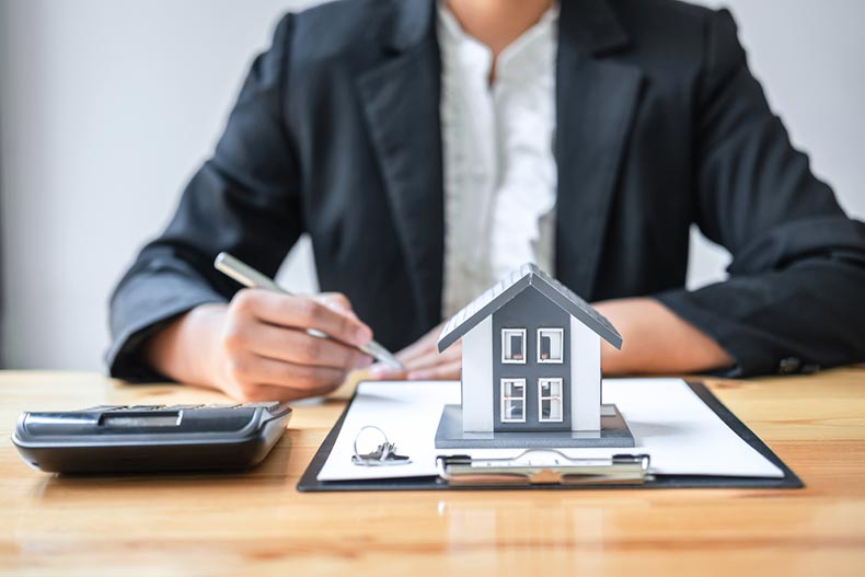 A real estate agent with a home appraisal document on a clipboard, a model house, a calculator, and a key