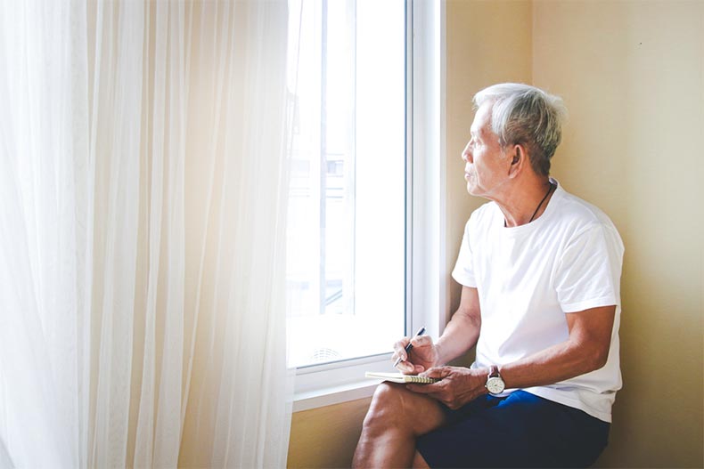 Older man sitting down looking out a window while writing