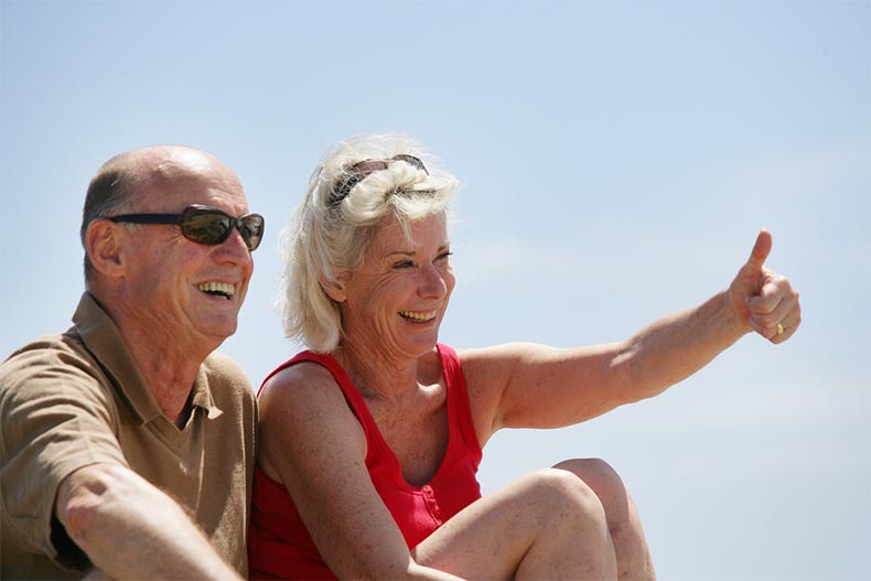 A laughing senior man sitting next to a smiling senior woman giving a thumbs up