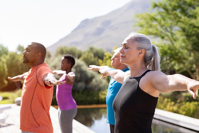 Senior people with closed eyes and outstretched arms doing yoga outdoors