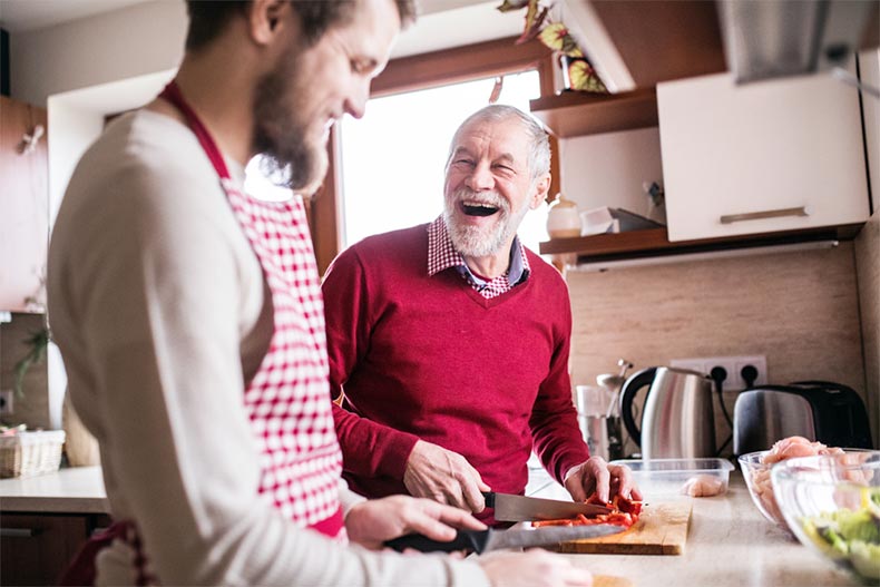 A senior man laughing while cooking in the kitchen with his adult son